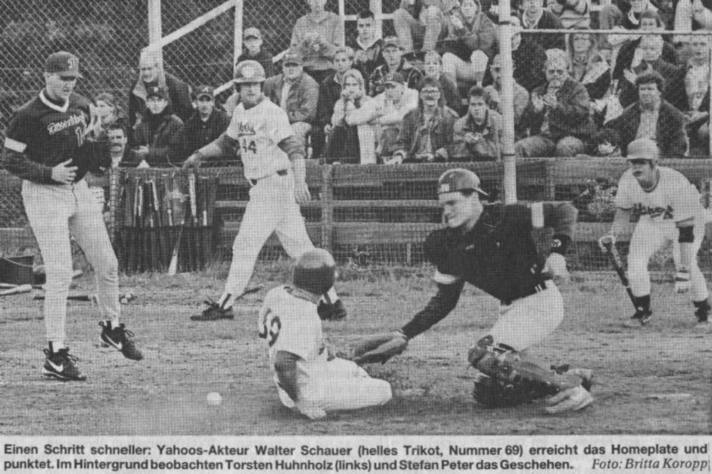 Einen Schritt schneller: Yahoos-Akteur Walter Schauer (helles Trikot, Nummer 69) erreicht das Homeplate und punktet. Im Hintergrund beobachten Thorsten Huhnholz (links) und Stefan Peter das Geschehen. Foto: Britta Koropp